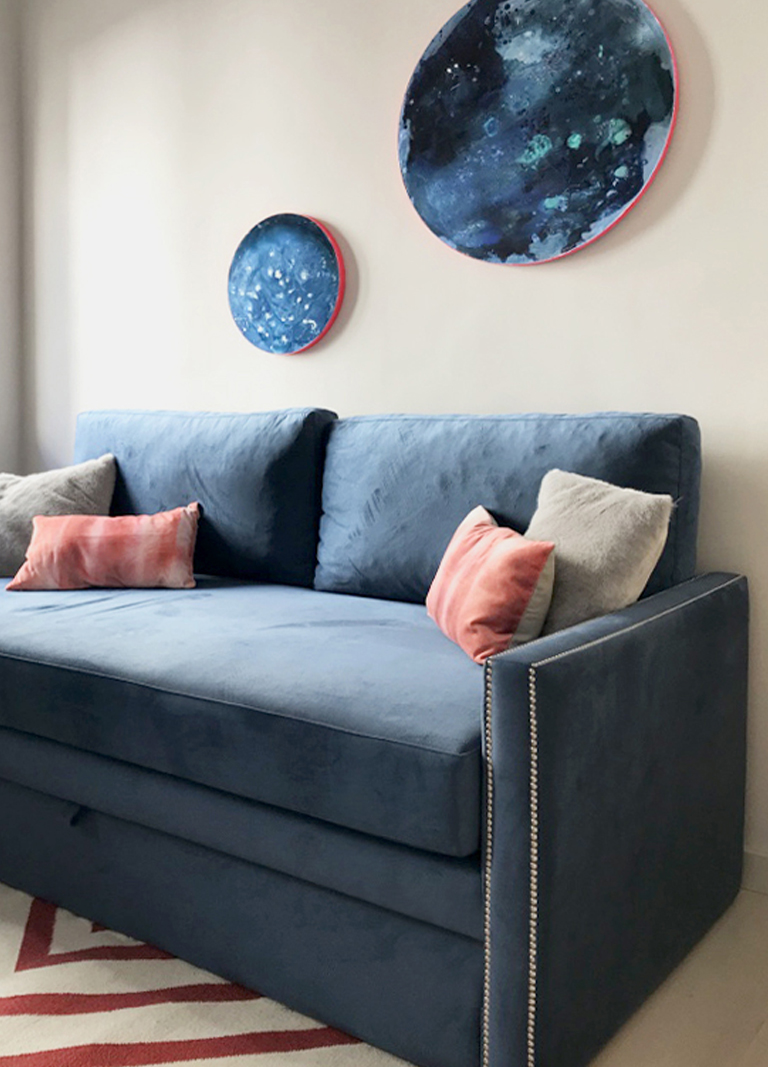 Sofá de terciopelo azul, cojines rosados, arte en pared