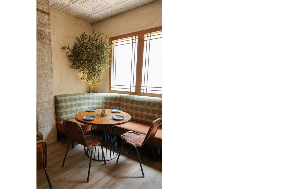 Detalle de interiorismo, banco corrido con tela a cuadros, mesa de tope de madera y estructura metálica, sillas de cuero