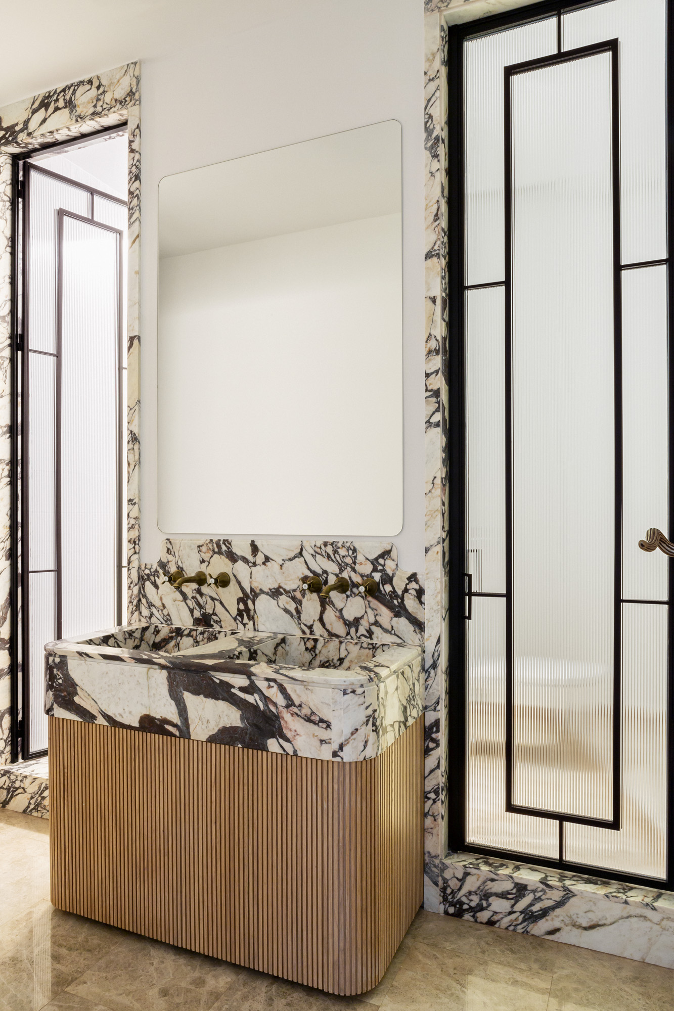 Reforma de baño principal con suelos de mármol ambarino, embocaduras de puertas en piedra Calacatta Viola, mueble en roble y encimera en piedra