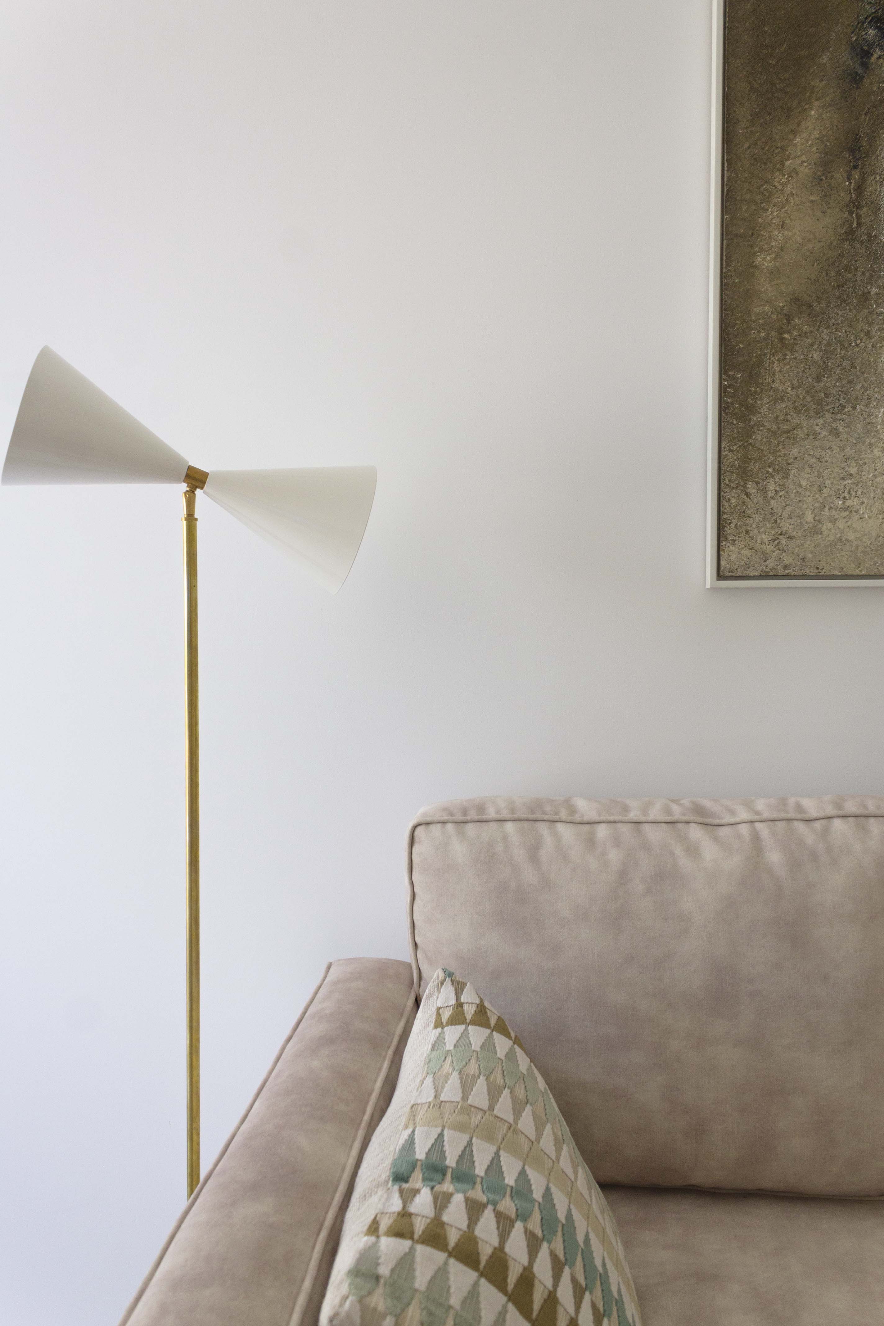 Foto de detalle de proyecto de interiorismo del despacho con sofá cama hecho a medida, lámpara dorada y blanca, cojines con tela con motivo geométrico y cuadro de arte